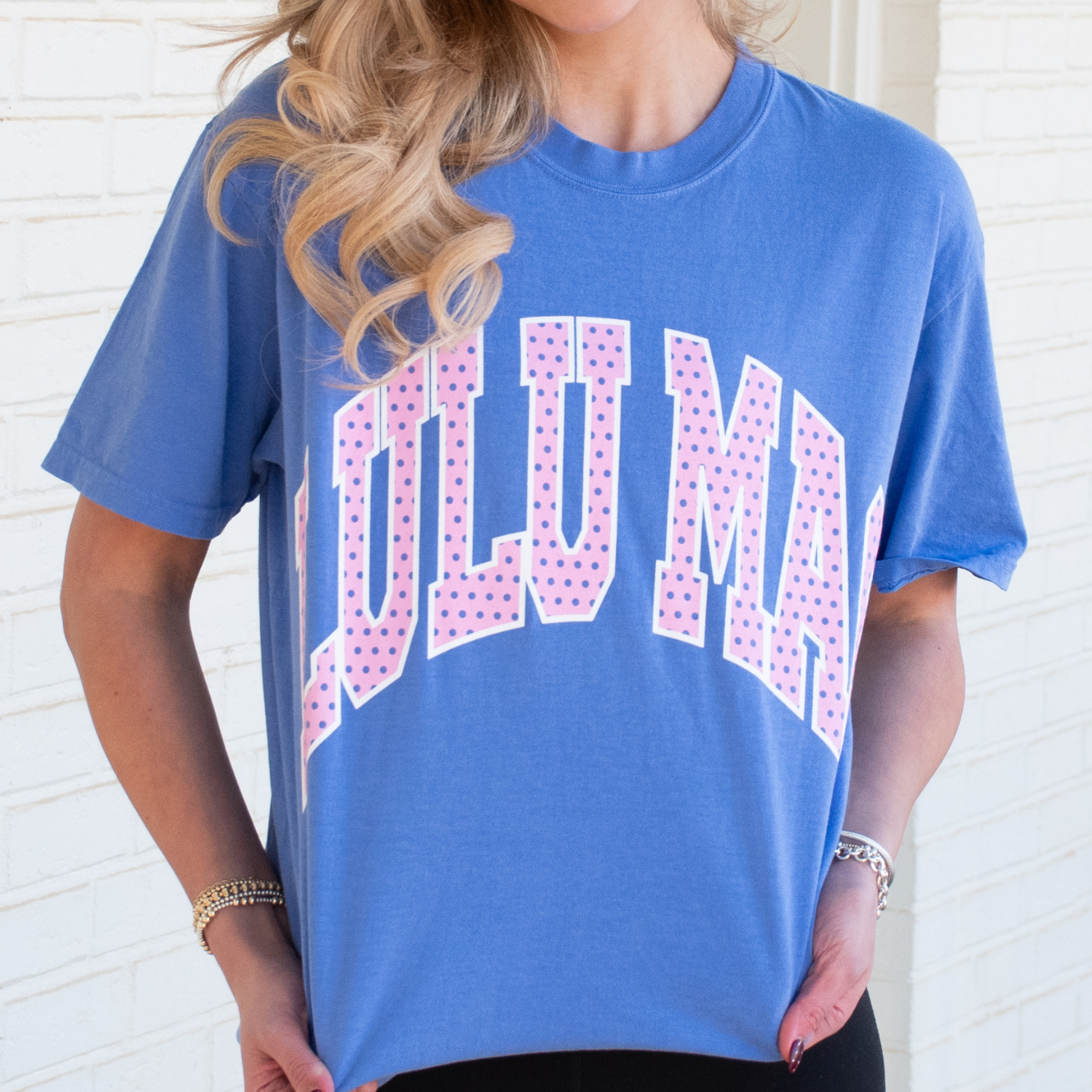 Person wearing a blue t-shirt with Lulumac printed on it against a white brick wall.