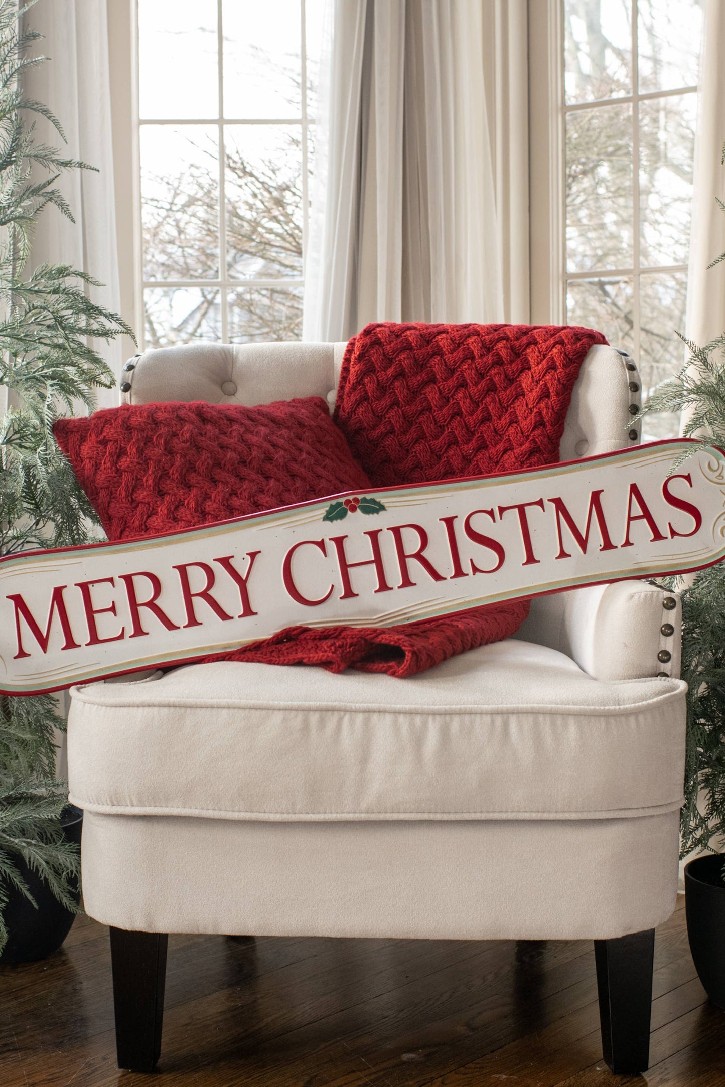 White armchair with red cushions and a 'Merry Christmas' sign, surrounded by Christmas trees.