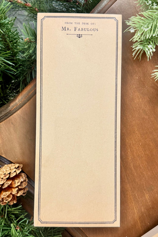 Notepad with 'From the Desk of Mr. Fabulous' text on a wooden surface with greenery