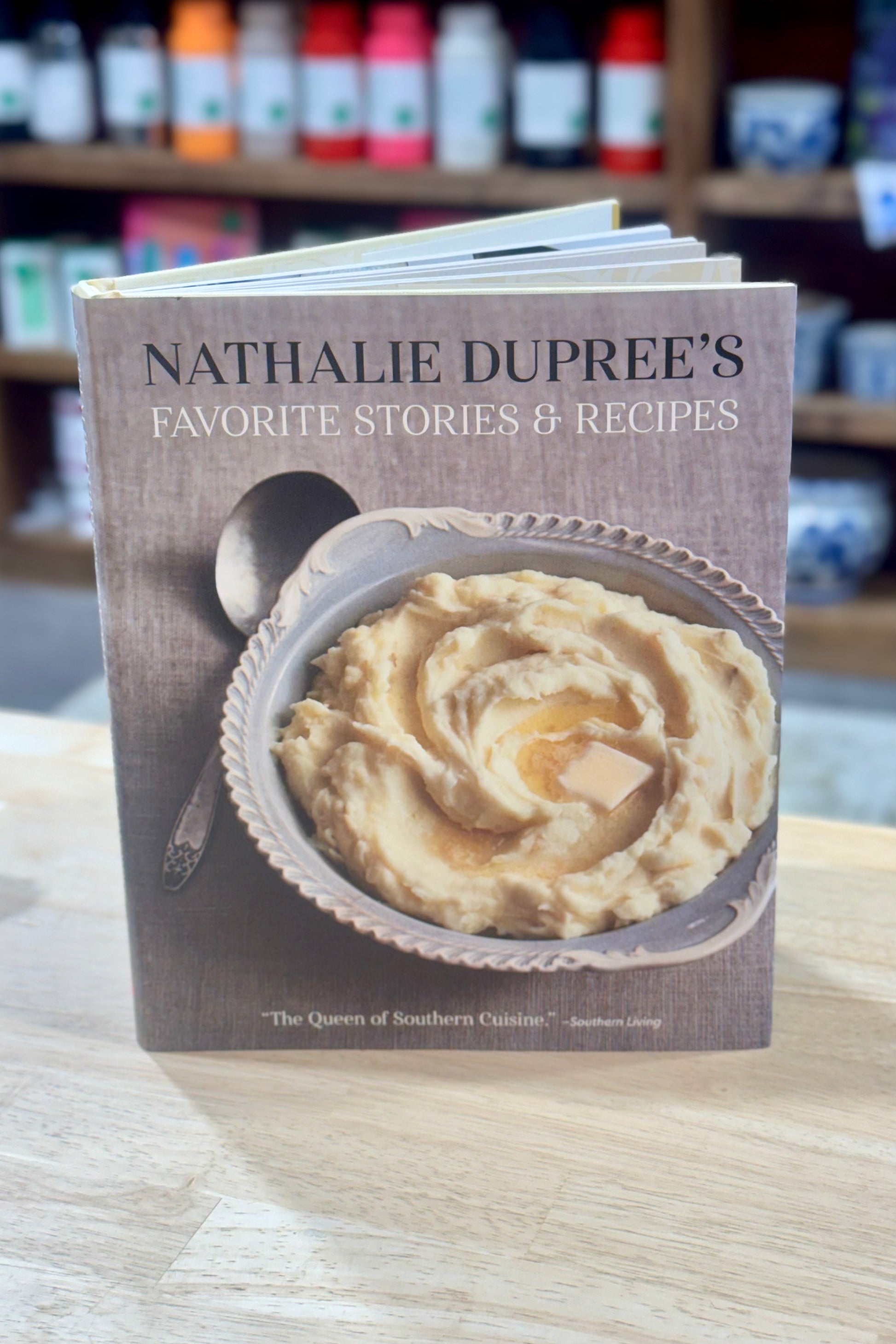 Book titled 'Nathalie Dupree's Favorite Stories & Recipes' on a wooden surface with a blurred background of shelves.
