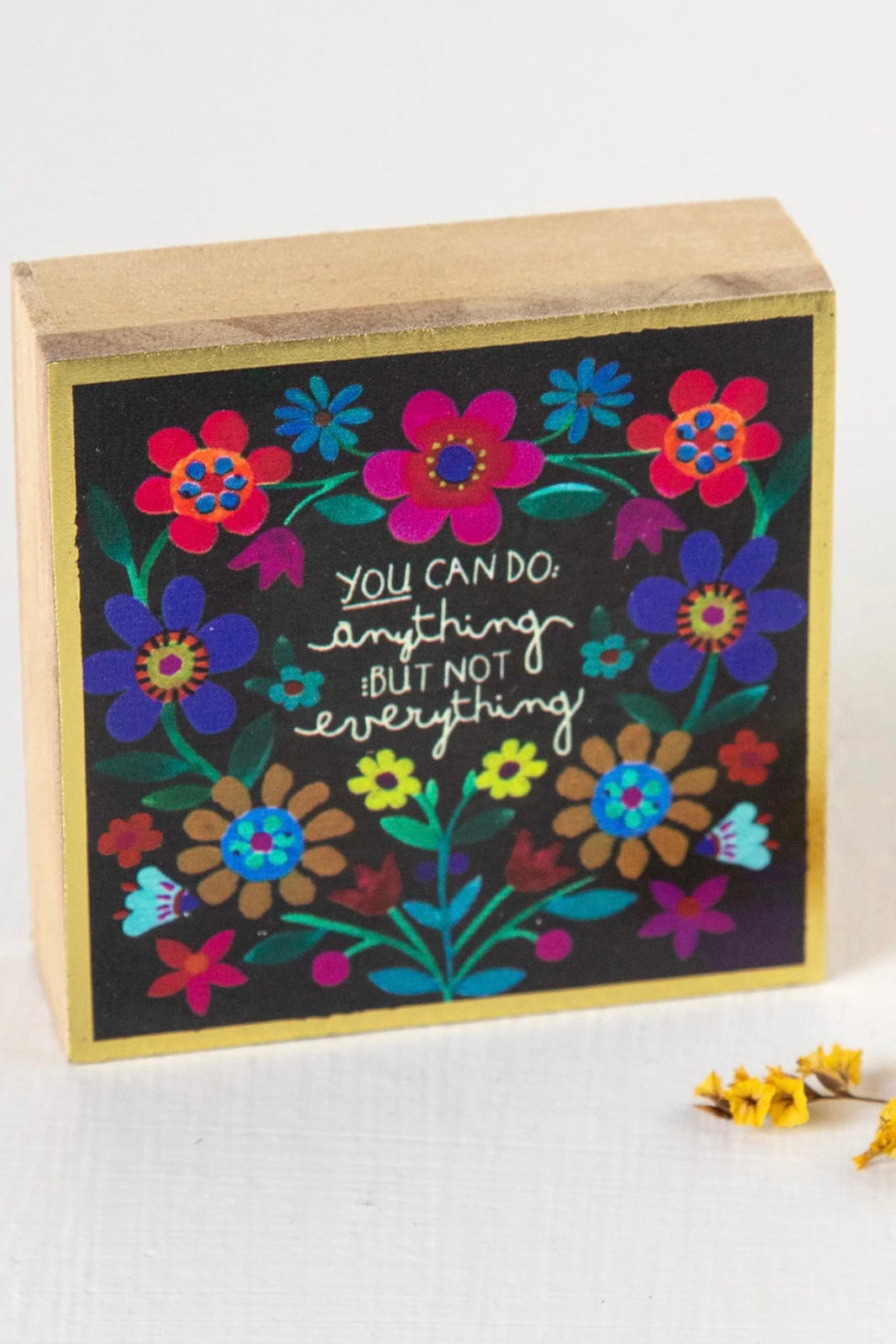 A decorative box sign with a floral design and the text 'You can do anything else' surrounded by colorful flowers, housed in a stained wooden frame with gold details.
