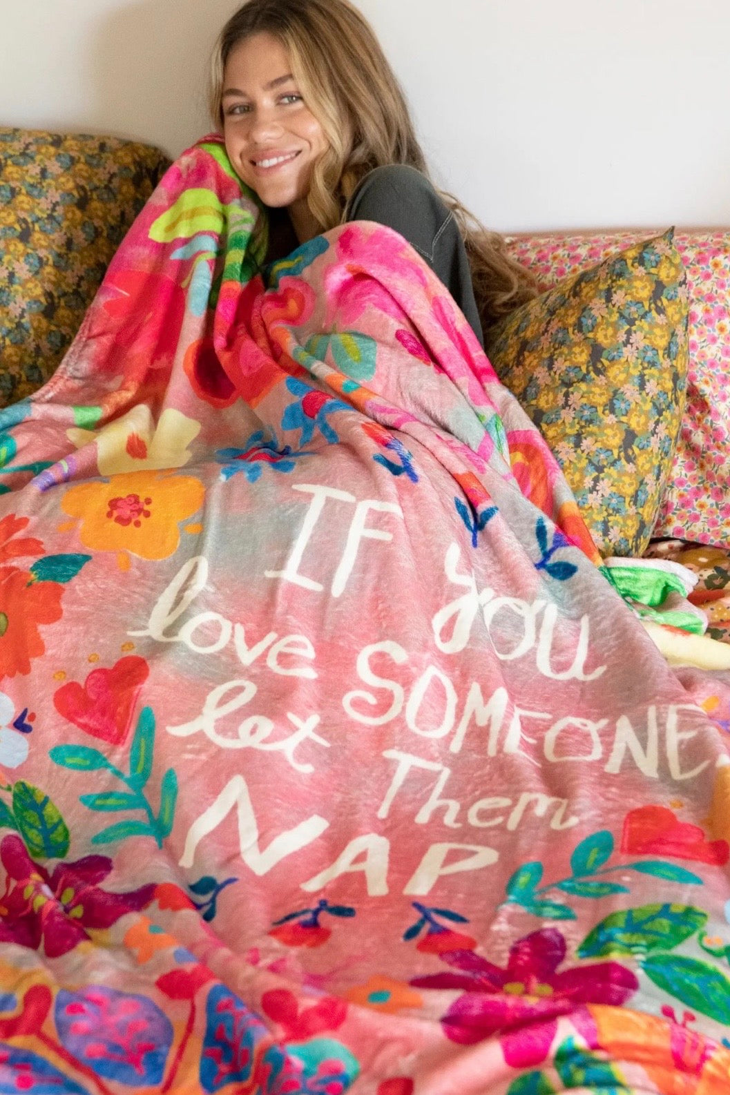Woman wrapped in a colorful blanket with text, sitting on a couch.