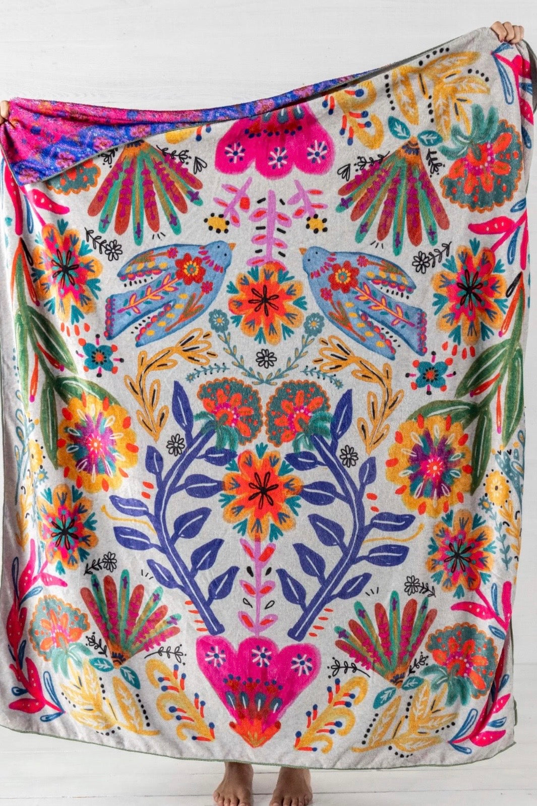 Colorful floral and bird patterned fabric draped over a person against a white background