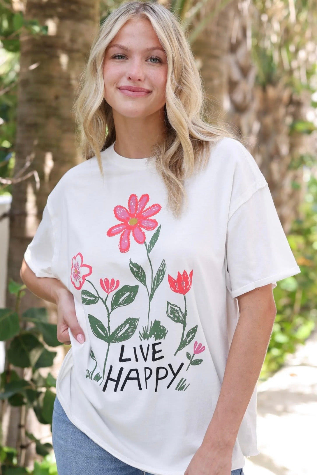 Person wearing a white t-shirt with floral design and 'Live Happy' text outdoors.