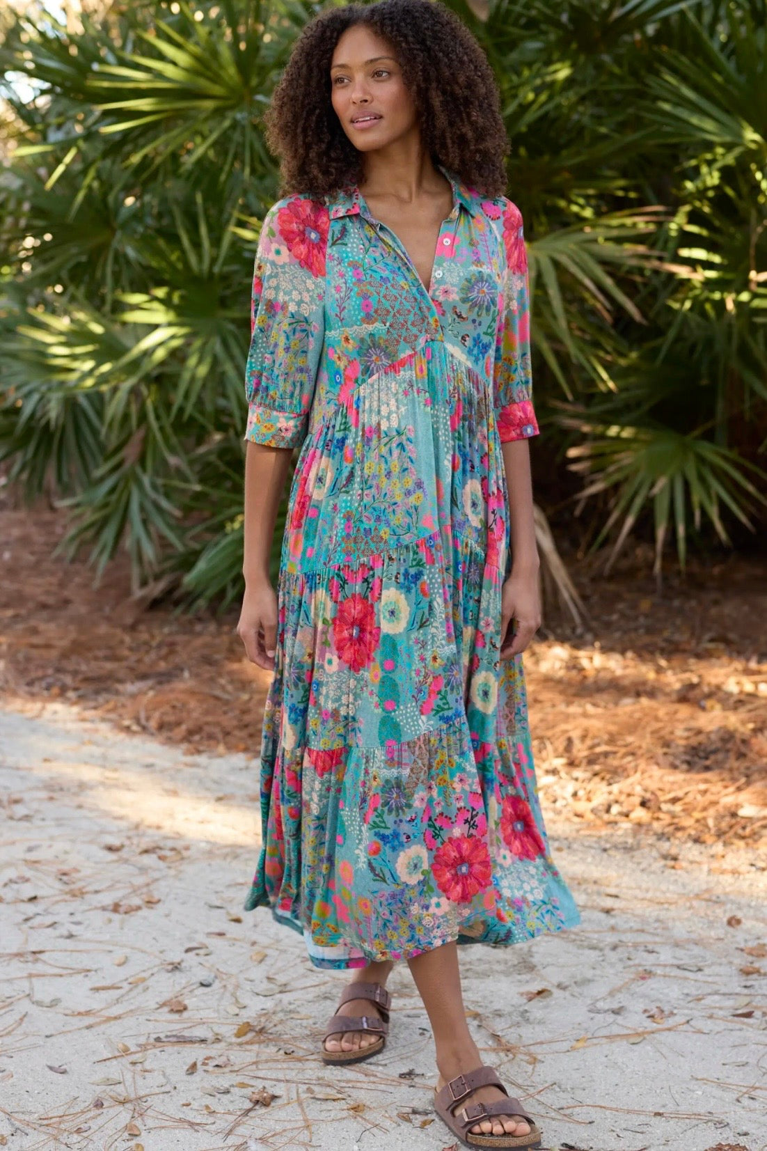Woman wearing a colorful floral dress standing outdoors with greenery in the background