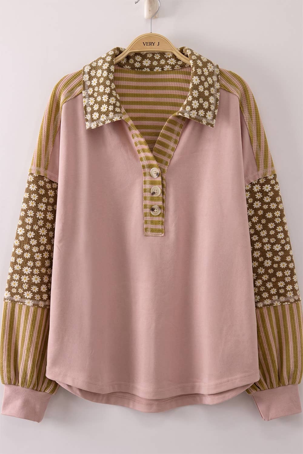 A women's long-sleeve polo shirt in blush pink, featuring contrasting patterned sleeves with vertical stripes and floral prints, and a matching patterned collar and placket.
