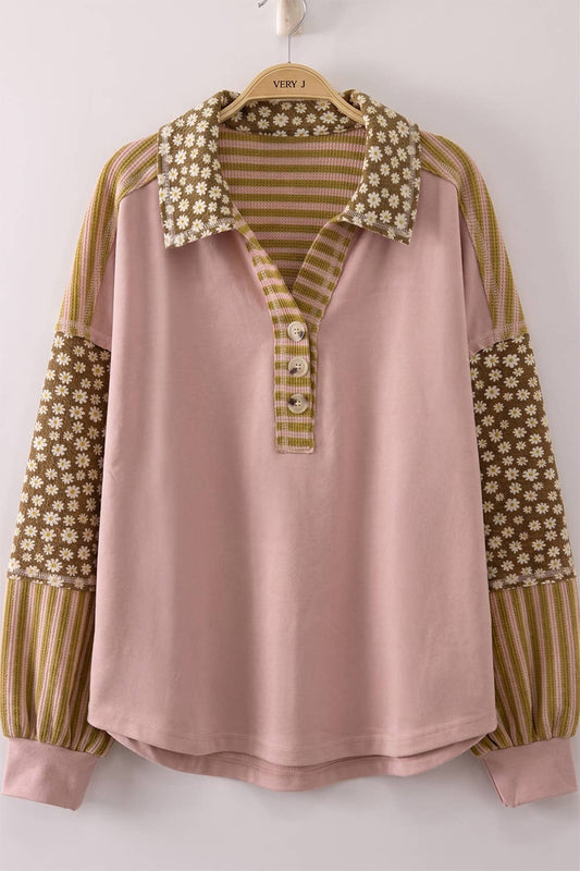 A women's long-sleeve polo shirt in blush pink, featuring contrasting patterned sleeves with vertical stripes and floral prints, and a matching patterned collar and placket.