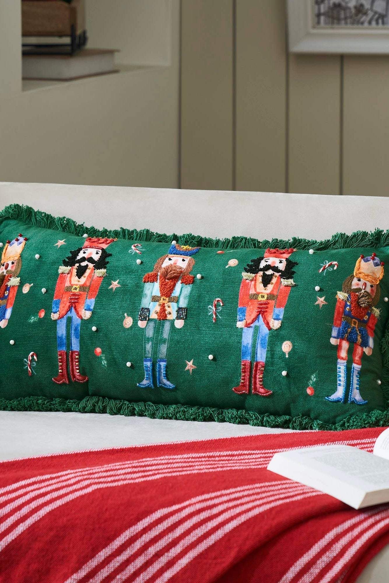 Decorative pillow with embroidered nutcrackers on a bed with red and white bedding.