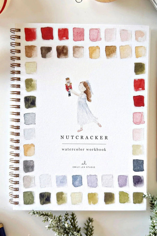 Watercolor workbook titled 'Nutcracker' with a pen and Christmas decorations on a white surface