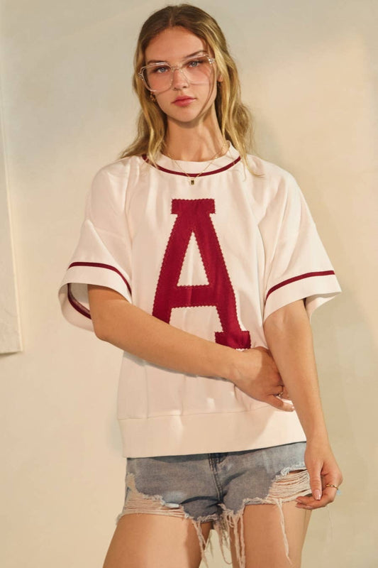 Person wearing a white t-shirt with a red 'A' and denim shorts against a plain background