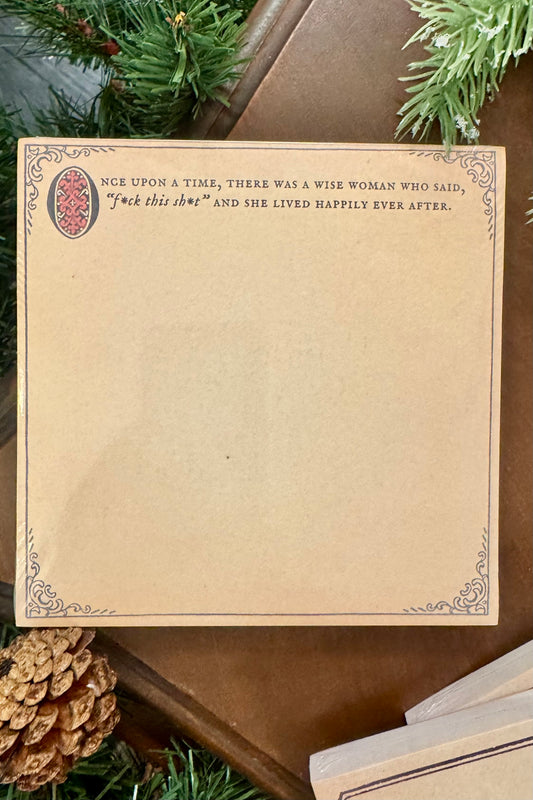 Decorative paper with text and decorative elements on a wooden surface with greenery.