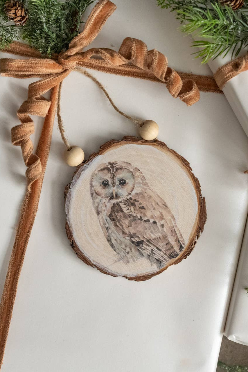 Wooden owl ornament on a wrapped gift with brown ribbon and greenery