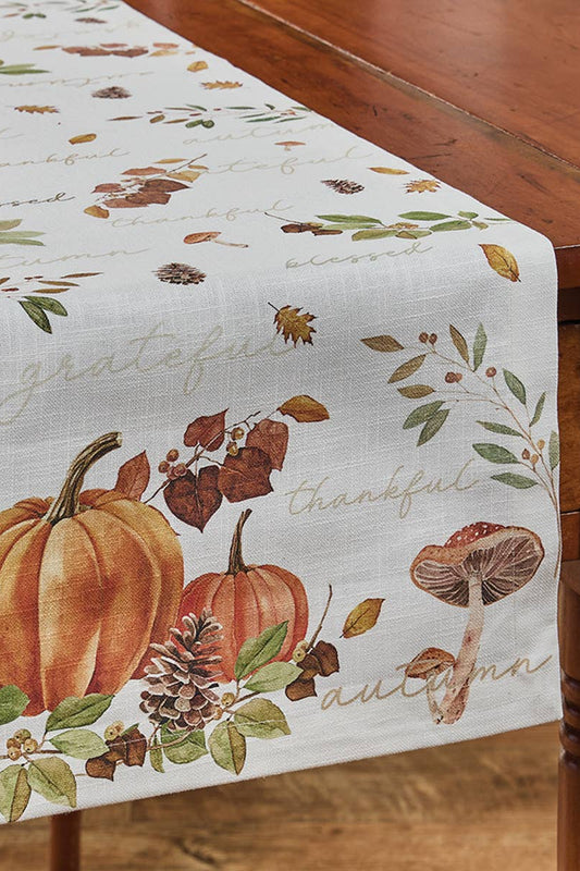 Autumn-themed table runner with pumpkins, leaves, and mushrooms on a wooden table.