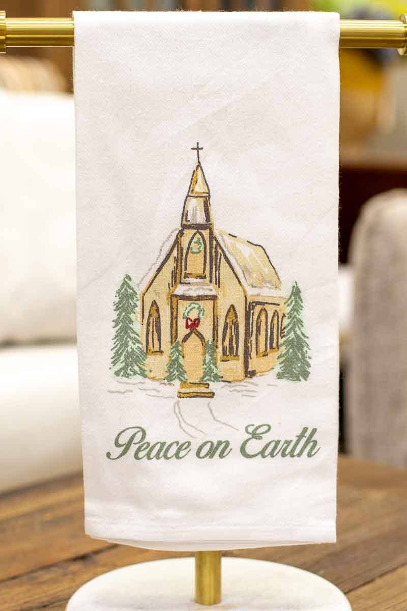 Decorative towel with a church design and 'Peace on Earth' text, hanging on a stand.