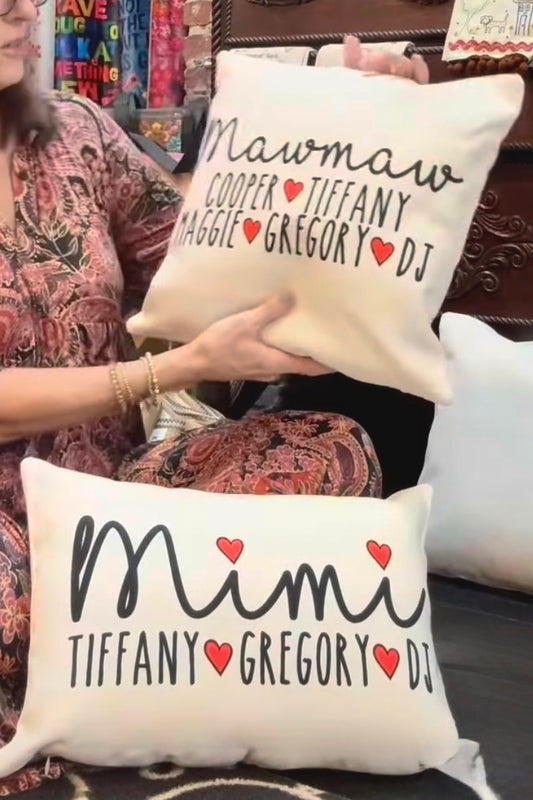Person holding two decorative pillows with personalized names and heart designs.