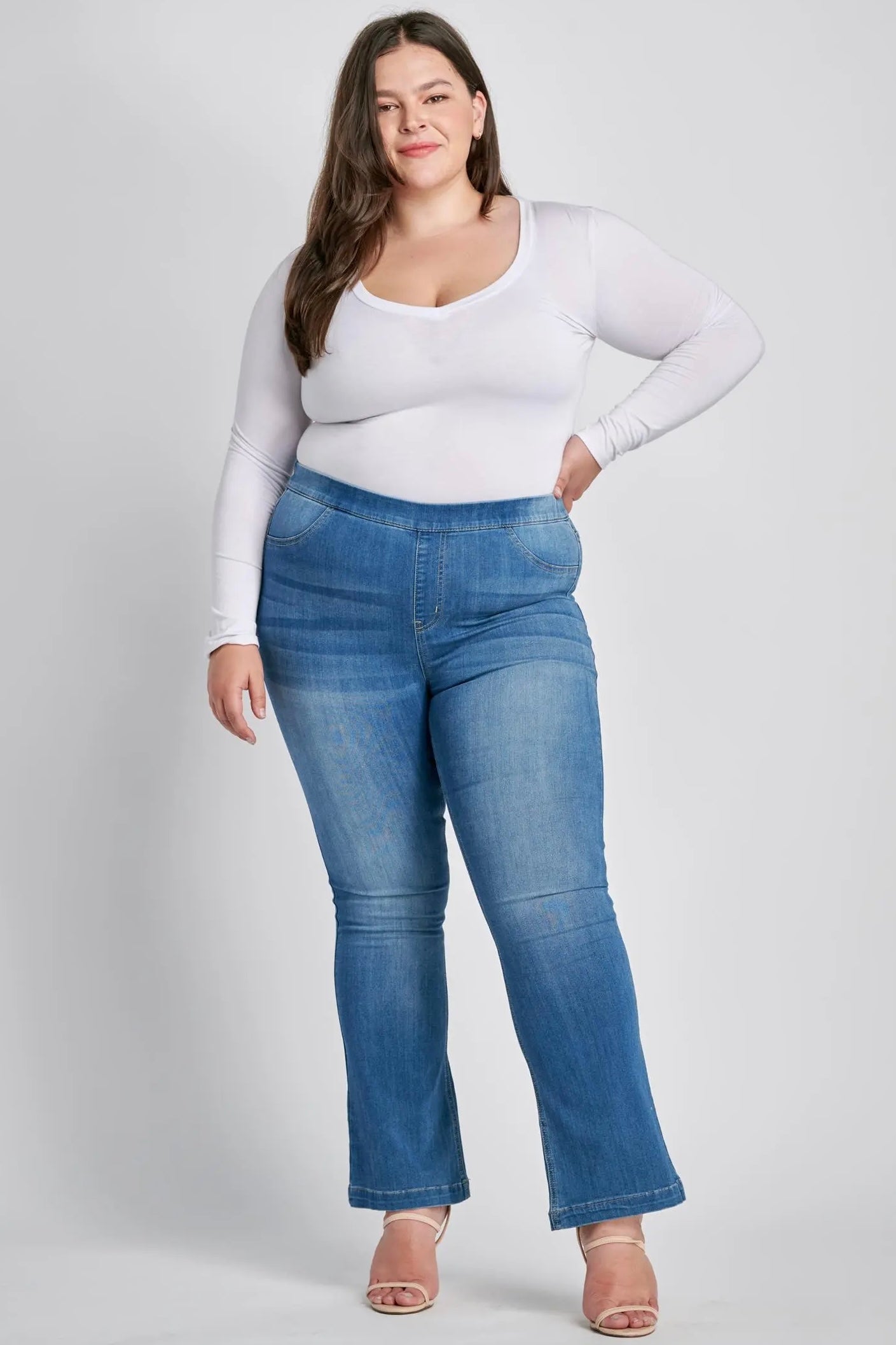 Woman wearing cELLO blue jeans and a white long-sleeve top on a plain background