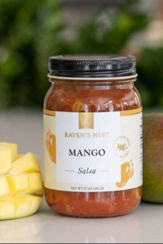 Jar of Mango Salsa on a kitchen counter with mango pieces and a blurred background