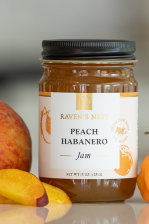 Jar of Peach Habanero jam with peaches and habanero peppers on a reflective surface.