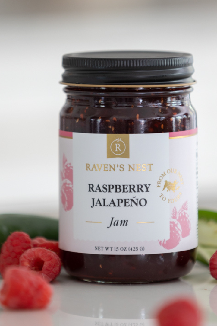 Jar of raspberry jalapeño jam with raspberries and jalapeños on a white background