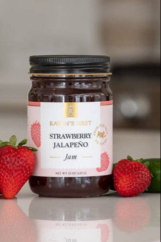 Jar of strawberry jalapeno jam on a countertop with strawberries and a jalapeno pepper.