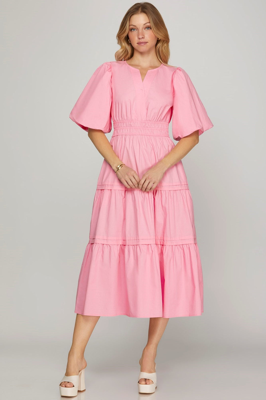 Woman wearing a pink dress with ruffled sleeves on a gray background