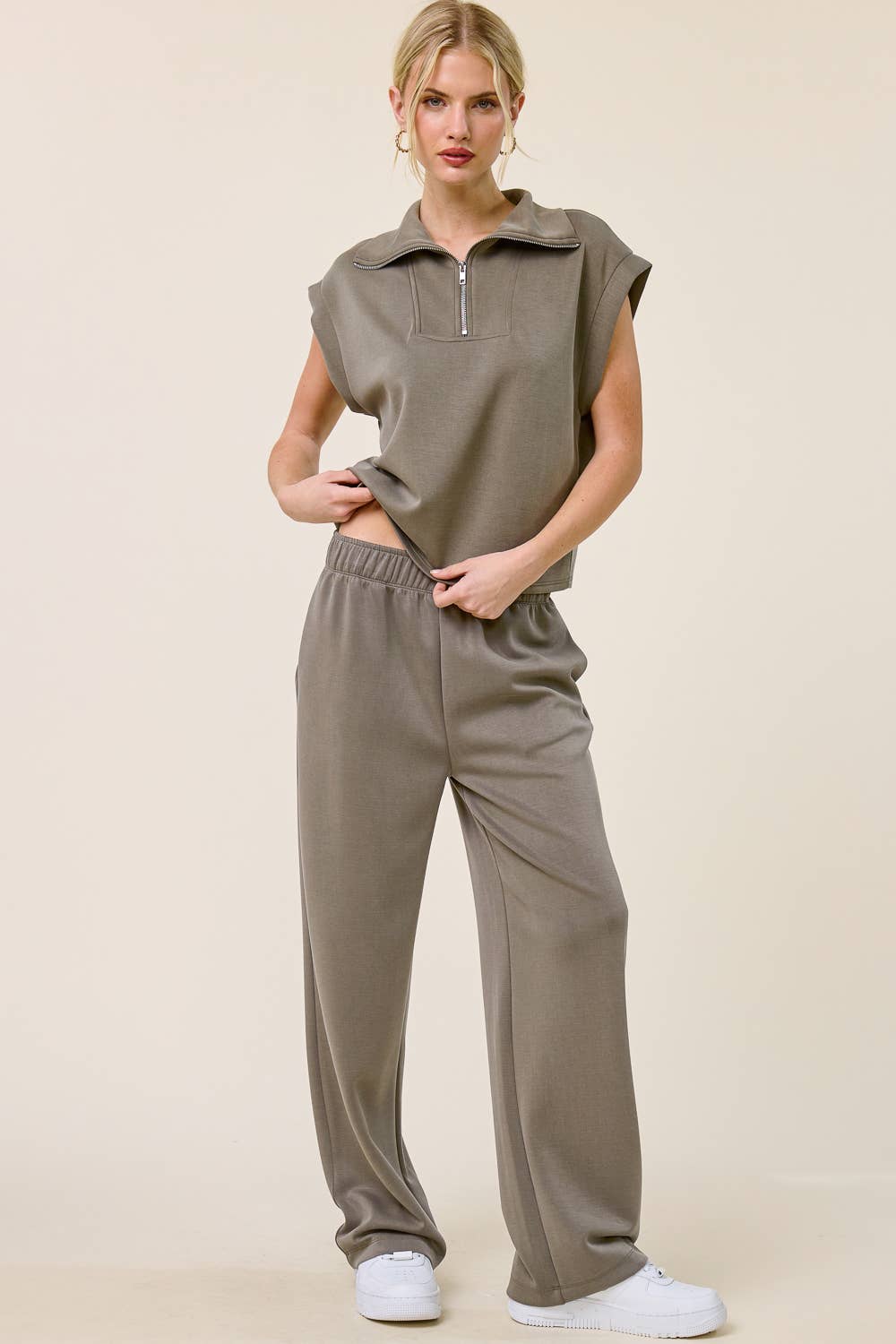 Woman wearing a beige sleeveless top and pants on a beige background