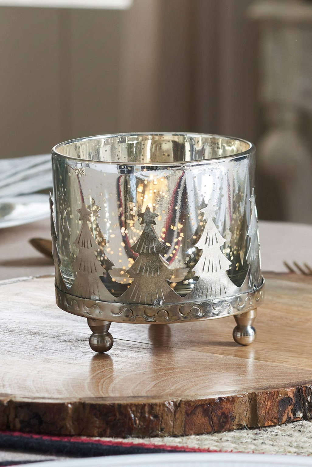 Decorative glass candle holder on a wooden board with a festive setting