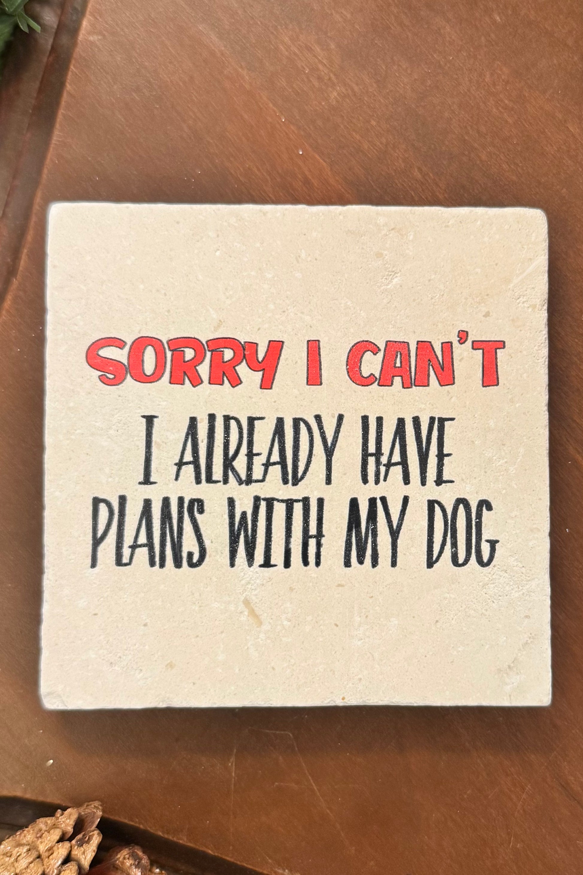 Square coaster with text 'Sorry I can't, I already have plans with my dog' on a wooden surface.