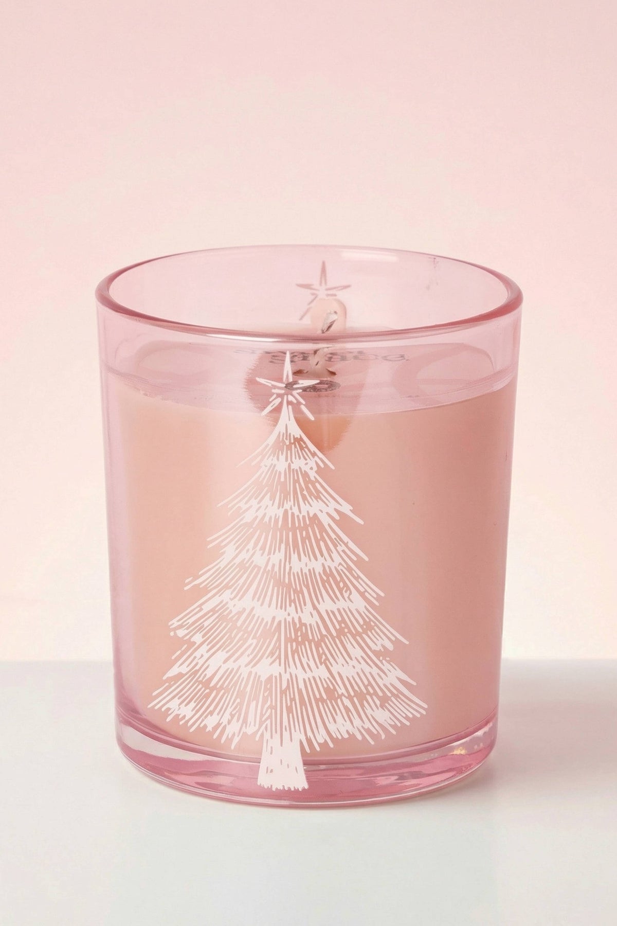 Pink candle with a white tree design on a light pink background