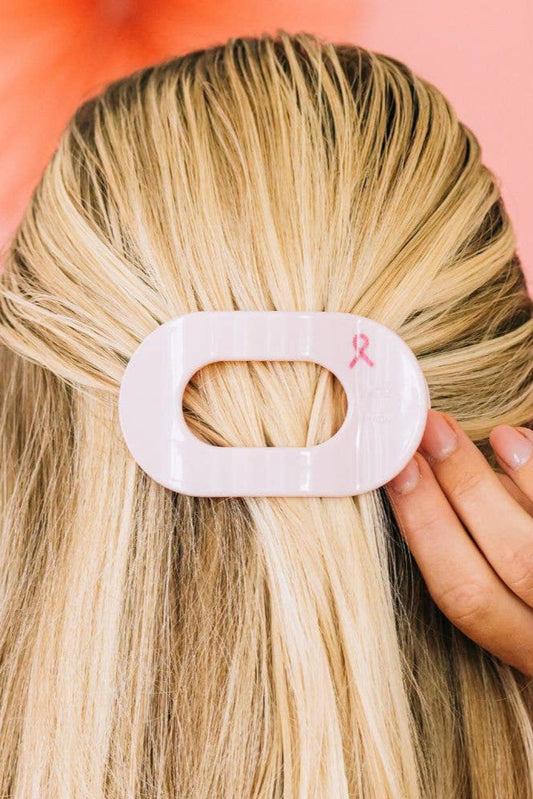 Person with blonde hair wearing a pink hair clip against a pink background