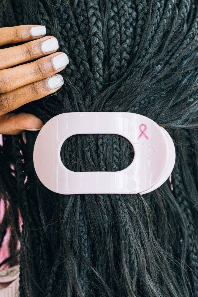Hair clip with a pink ribbon on braided hair, blurred background