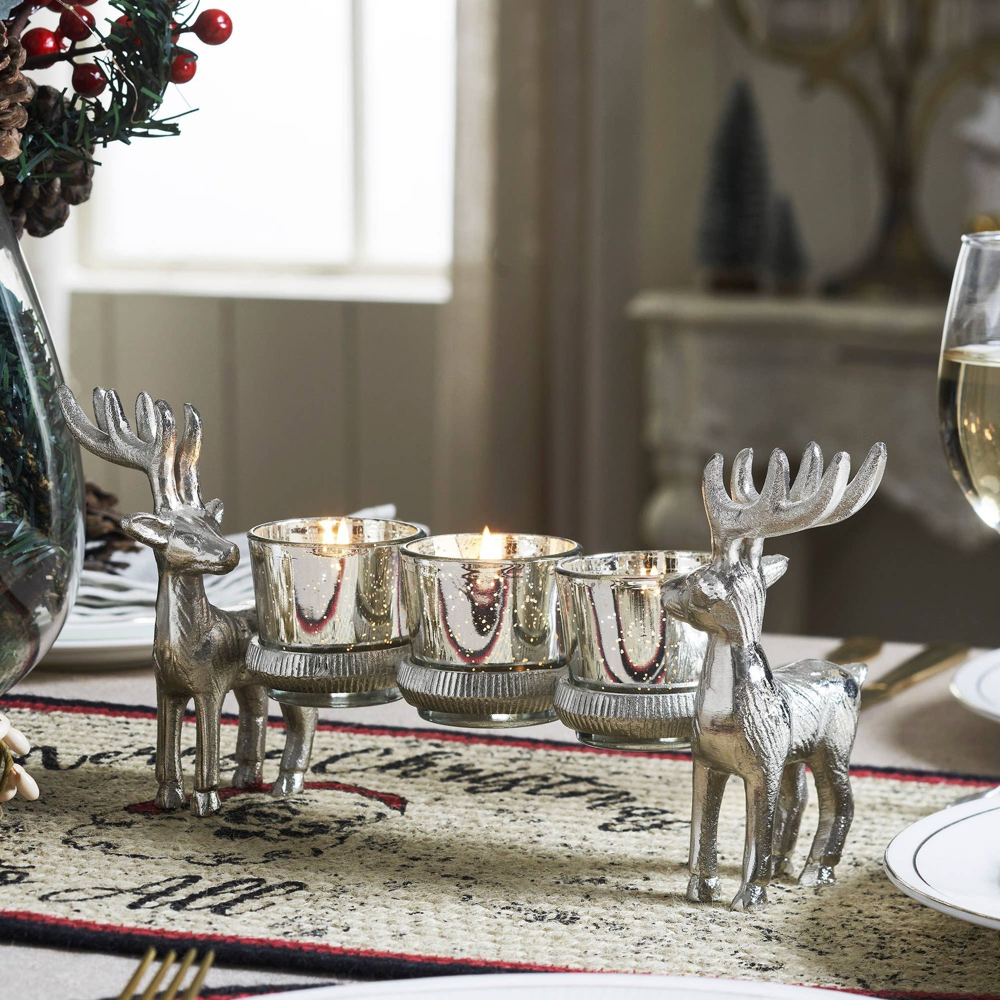Silver deer candle holders on a festive table setting with candles and a glass of wine.