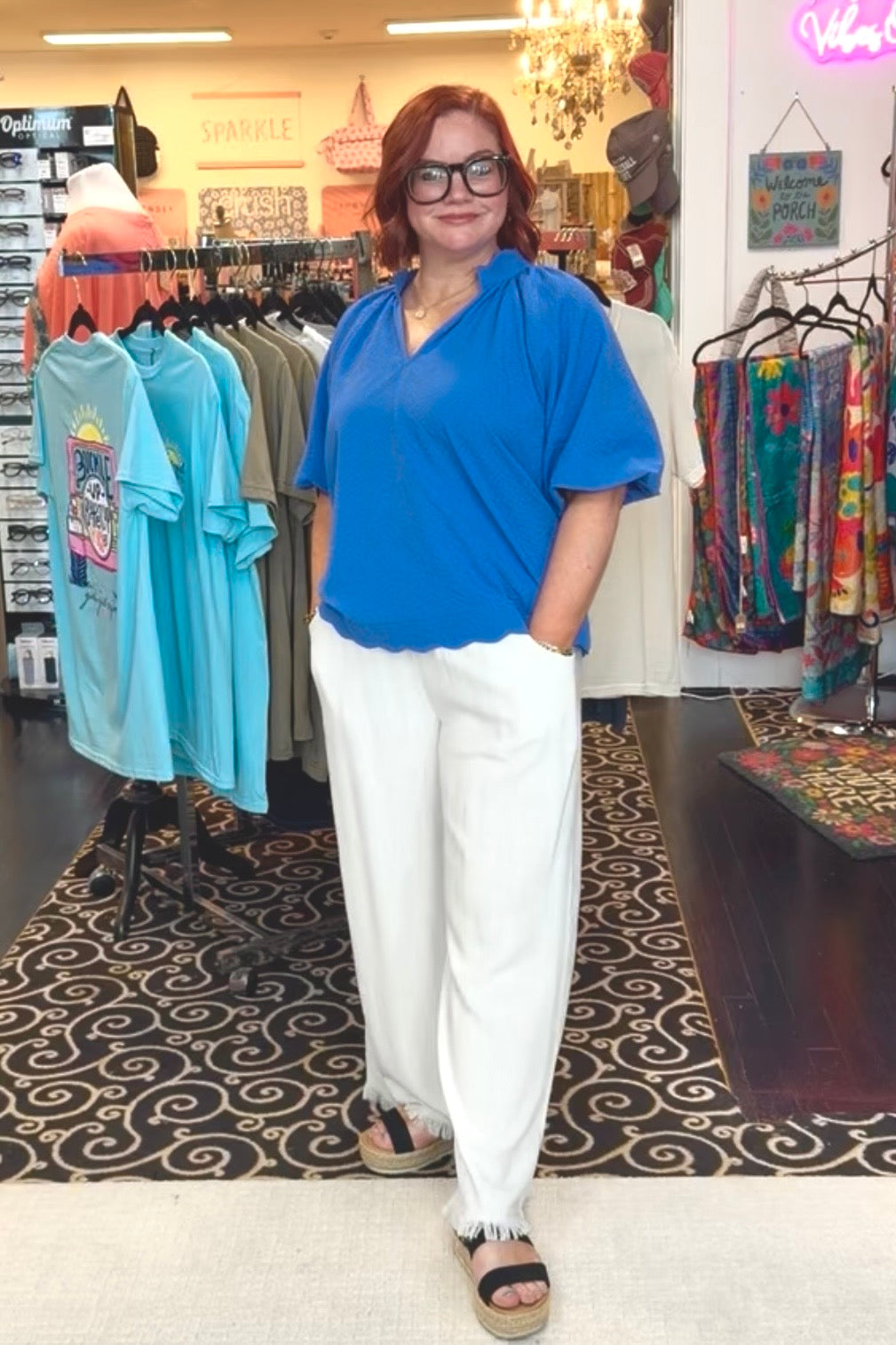 Woman in a blue shirt and white pants standing in a clothing store.