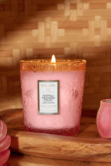 Two pink candles with decorative lids on a wooden tray against a woven bamboo background Voluspa Napali Passion Fruit 9 oz Classic Candle