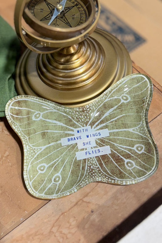 Butterfly-shaped decorative item with text on a wooden surface next to a brass compass.