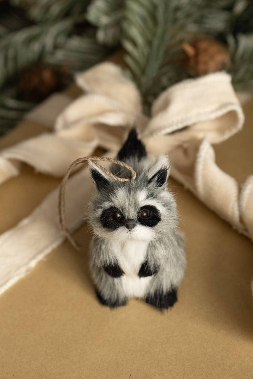 Fuzzy raccoon ornament on a brown surface with decorative ribbon