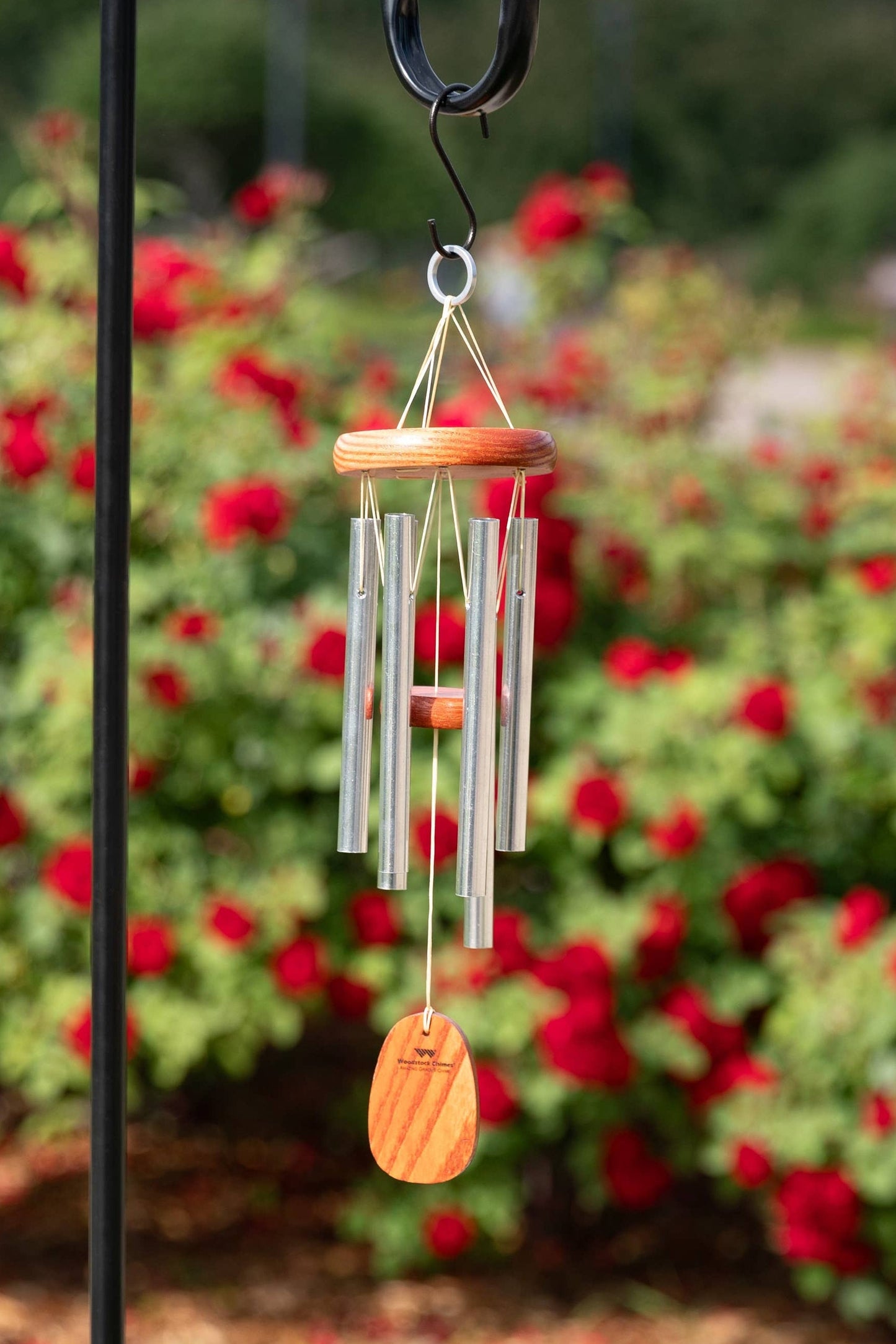 Wind chime on a stand with red flowers in the background