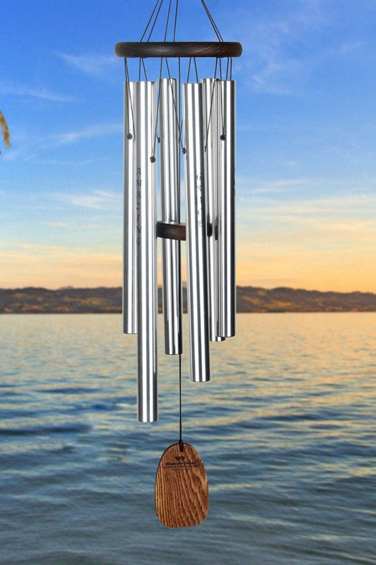 Silver wind chime with wooden finial hanging against a scenic lake and sky background