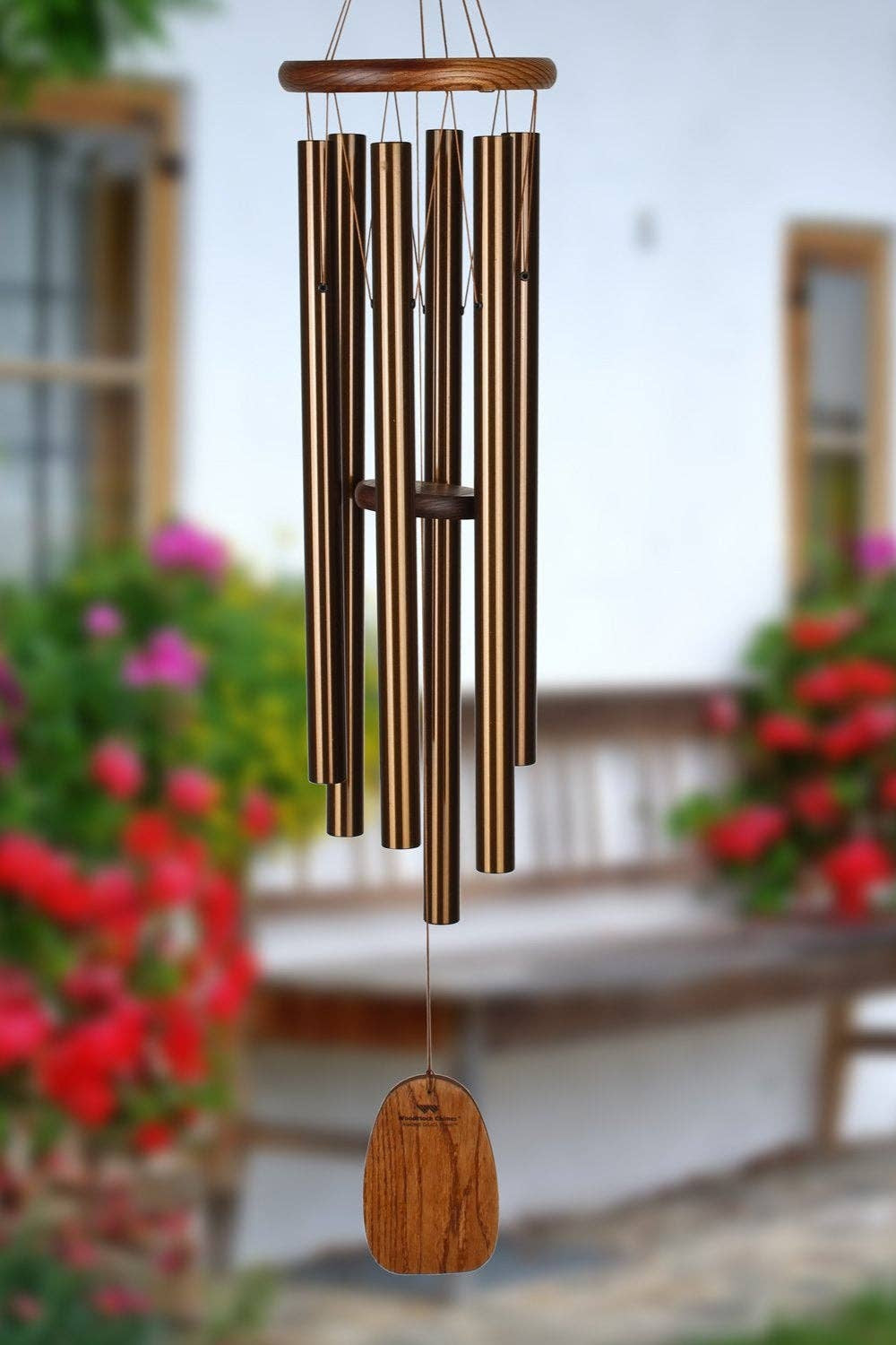 Bronze wind chime hanging in a garden with flowers and a wooden bench in the background