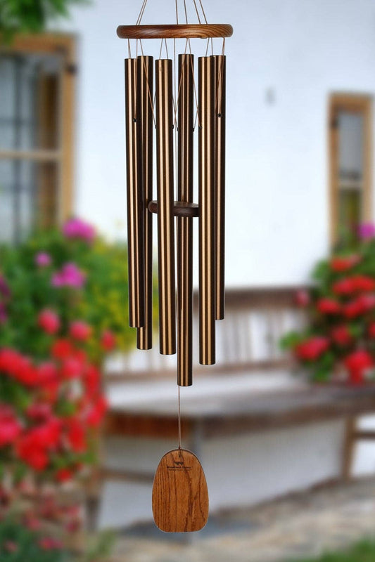Bronze wind chime hanging in a garden with flowers and a wooden bench in the background