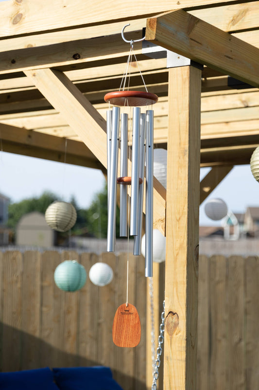 Decorative wind chimes hanging from a wooden pergola with a blurred garden background.