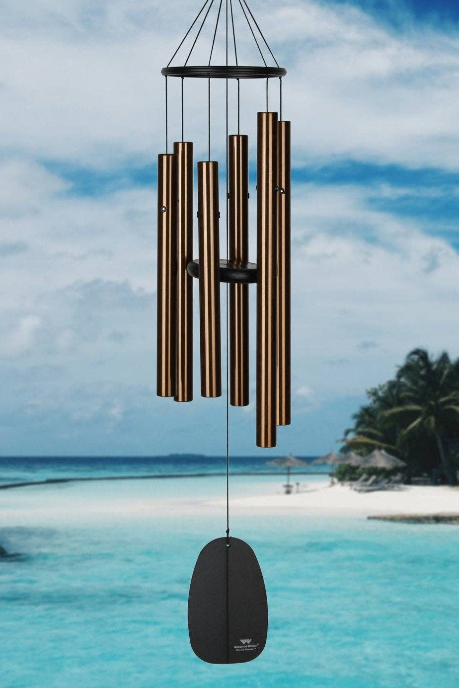 bronze and black Wind chime hanging over a tropical beach with turquoise water and white sand.