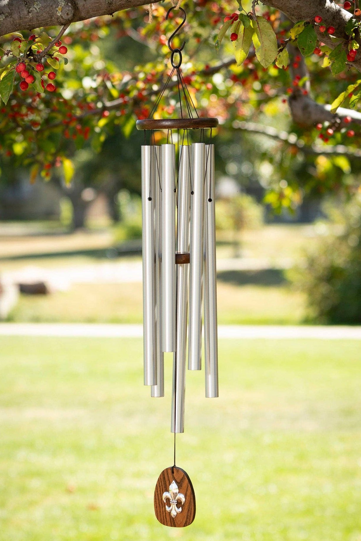 Silver wind chime hanging from a tree branch with greenery and grass in the background