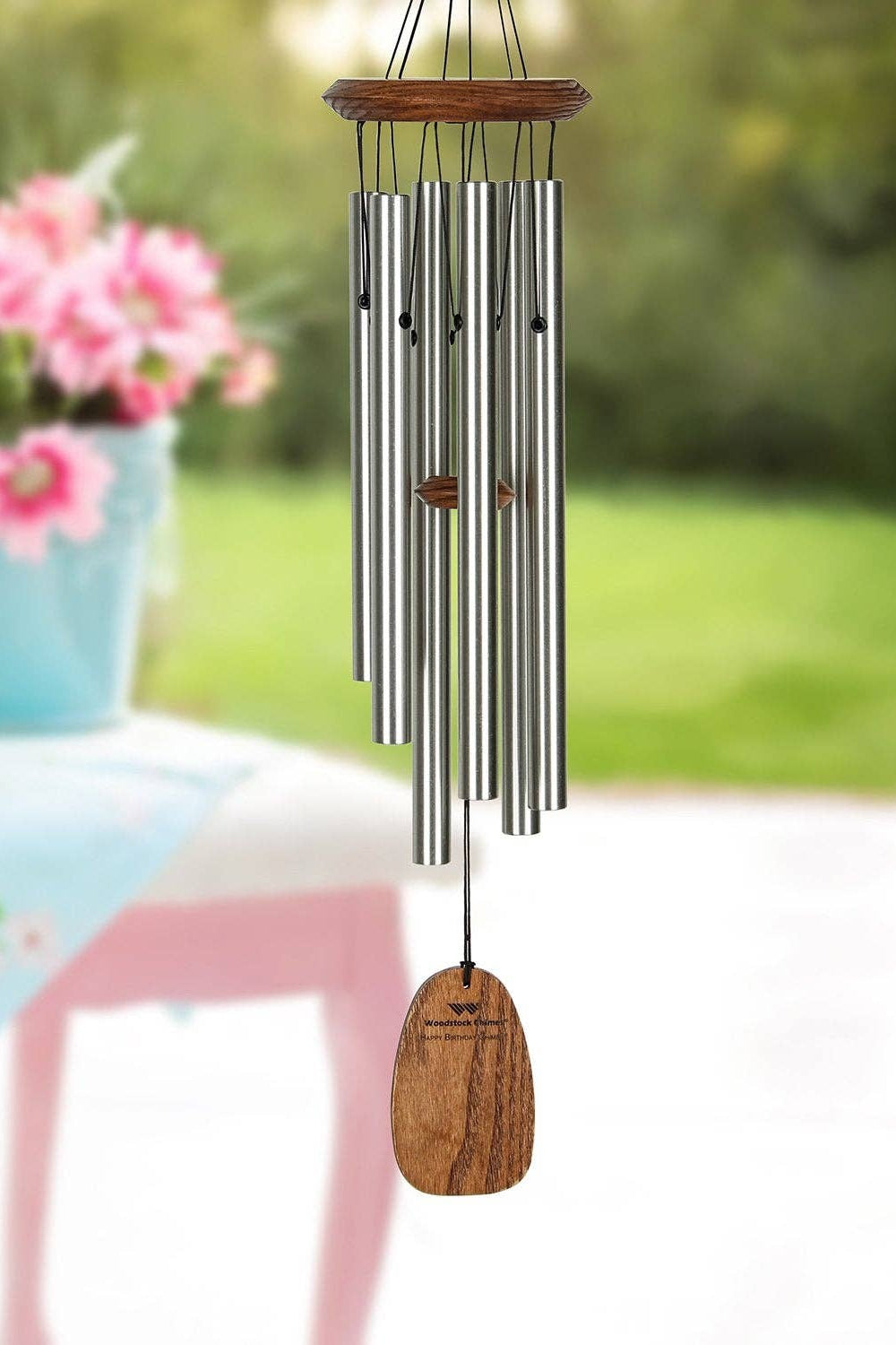 Decorative happy birthday wind chime with wooden accent on a garden table with flowers