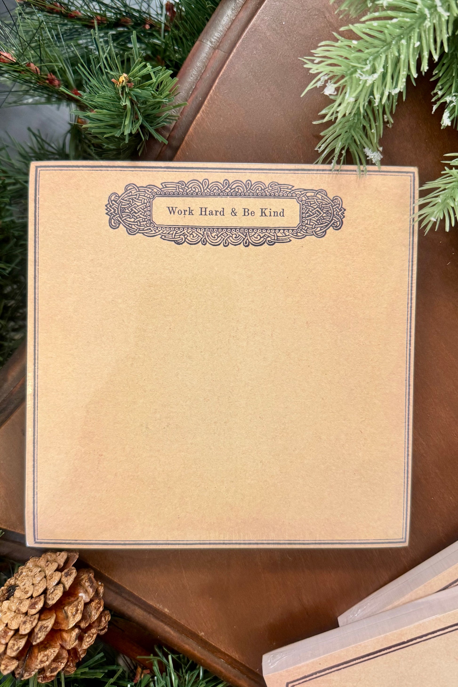 Notebook with 'Work Hard & Be Kind' text on a brown leather surface with greenery