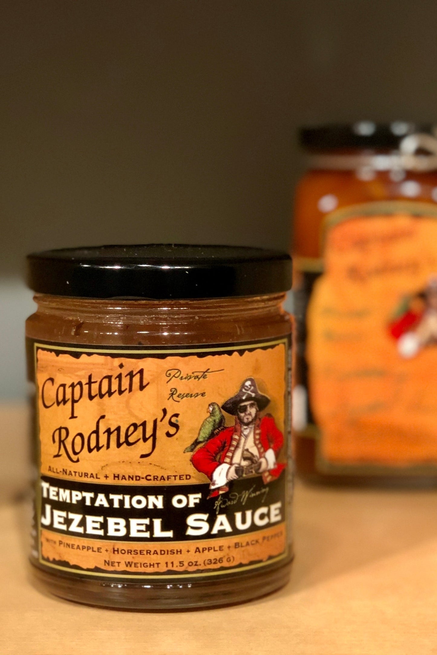 Jar of Captain Rodney's Temptation of Jezebel Sauce on a wooden surface with another jar in the background.