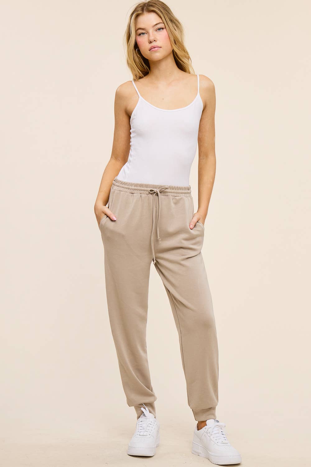 Woman wearing a white tank top and beige sweatpants on a beige background