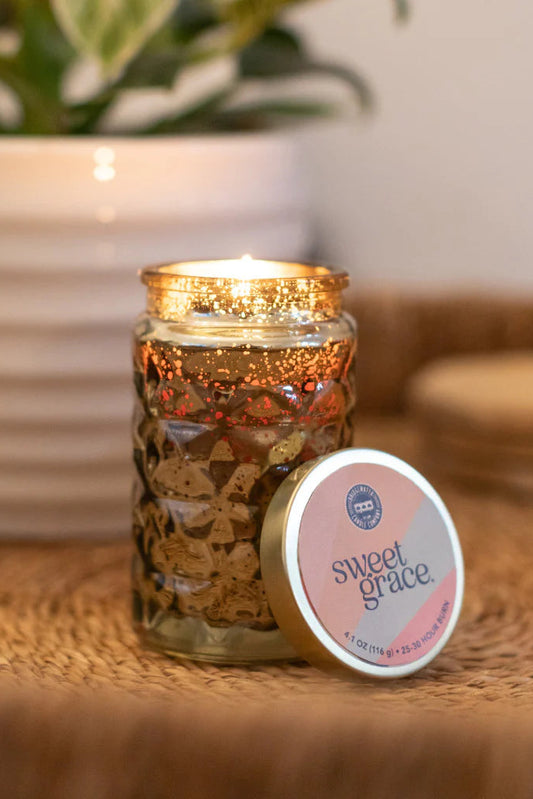 Candle in a decorative jar with 'sweet grace' label on a woven surface.