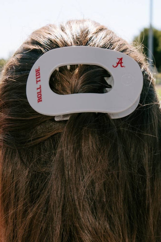 Person with a hair clip featuring 'Roll Tide' and a red letter 'A' on a blurred sports field background