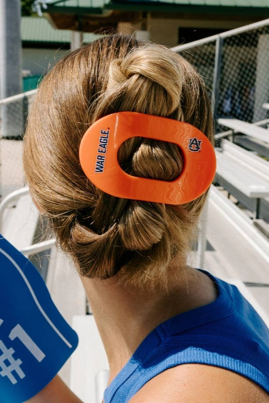 Person with an orange hair tie featuring a logo, sitting in bleachers.